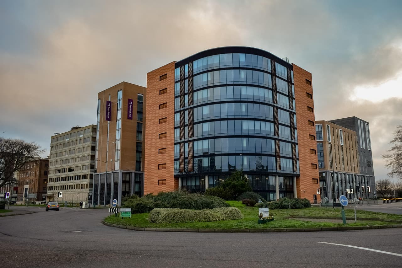 A roundabout planted with shrubs in front of a curved glass office block, under an evening sky