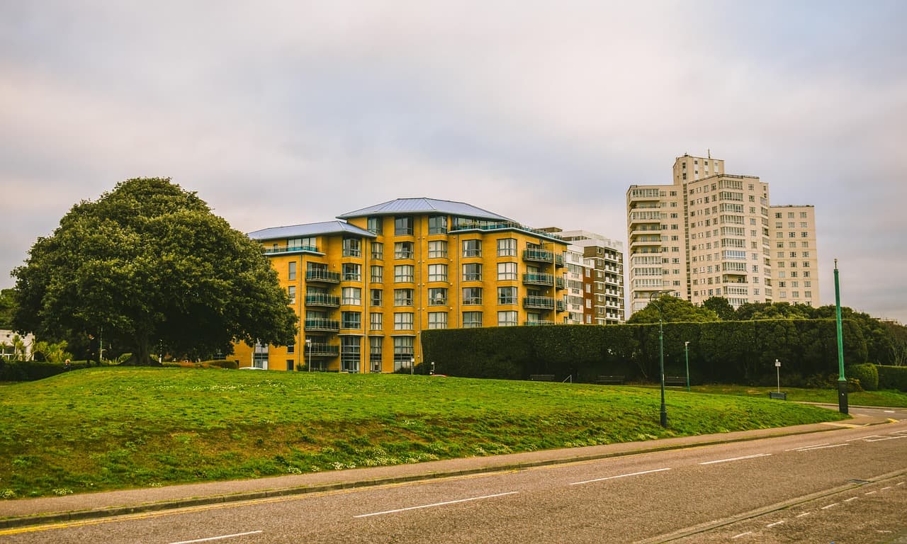 A road with wide grass verges and street trees running past modern flats